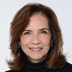 A woman with medium-length brown hair wearing a black turtleneck and small earrings, smiling softly at the camera against a plain light background.