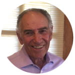 A portrait of an older man with graying hair wearing a light purple button-down shirt.